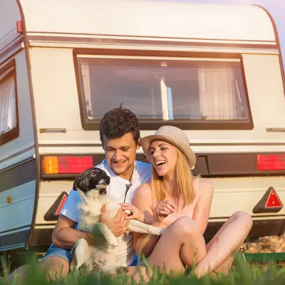 A couple outside their caravan with their dog watching the sunset